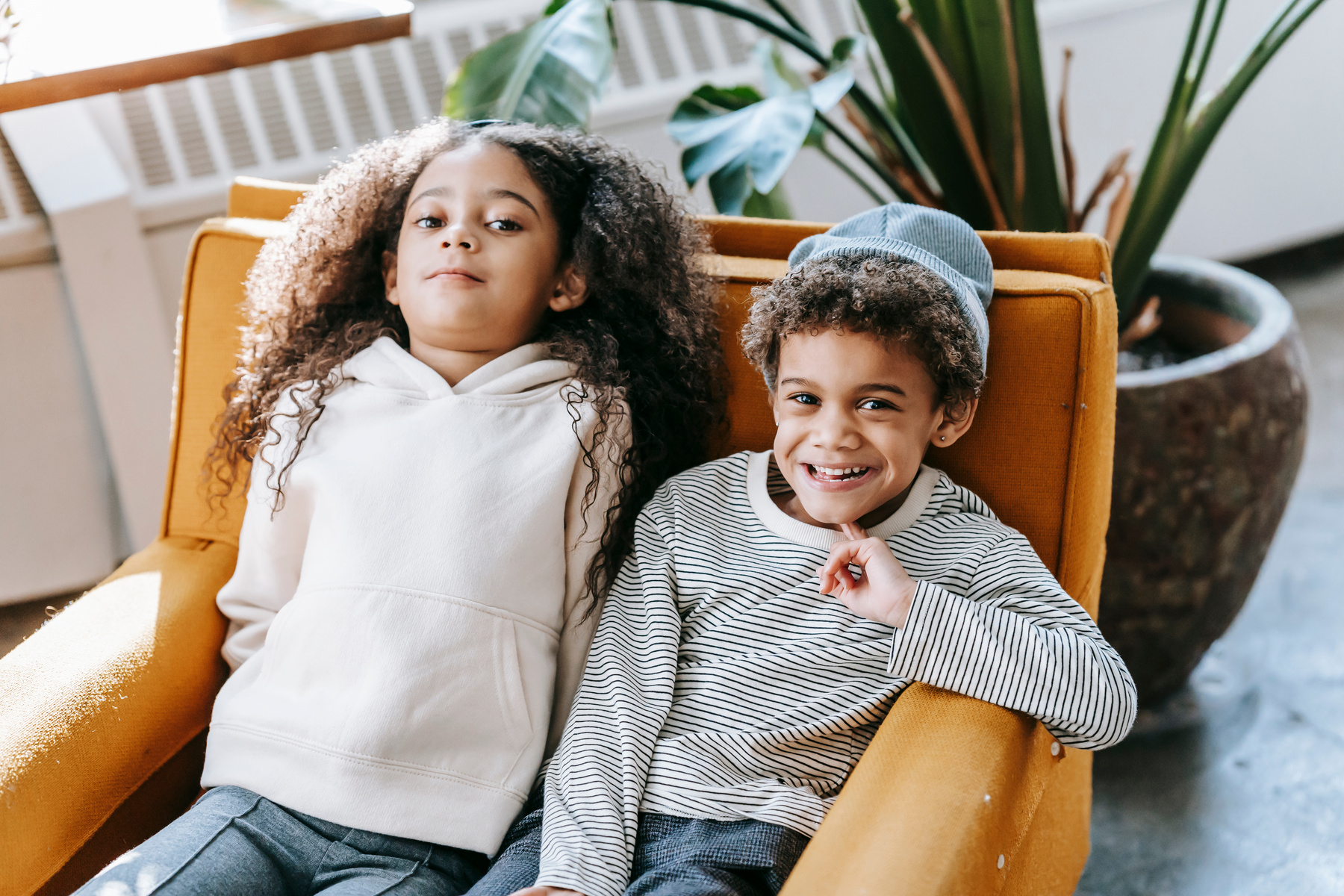 Cheerful black children in trendy clothes sitting on armchair at home